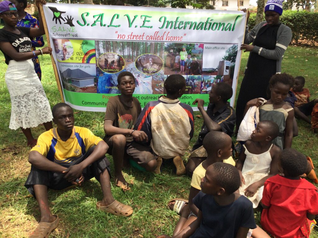 A group of children sat on the grass in front of a S.A.L.V.E international banner