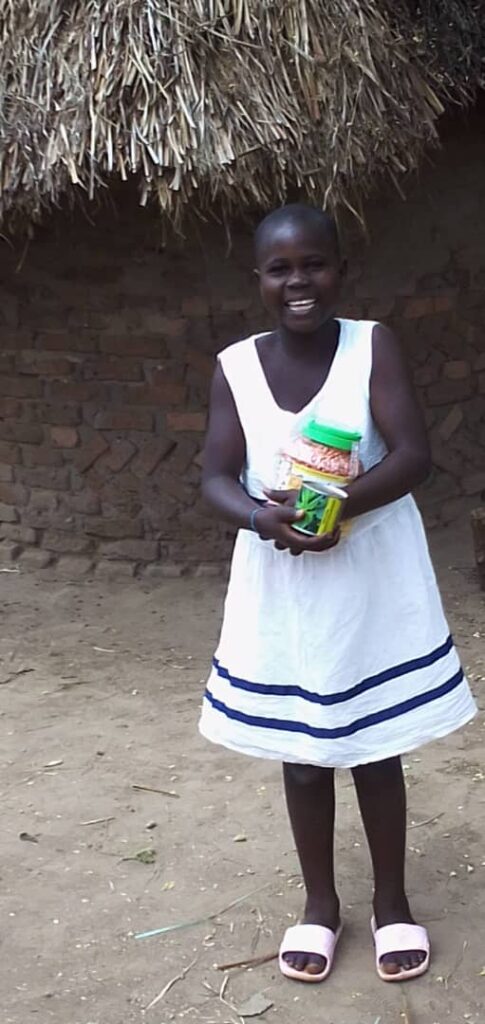 Viola smiling happily outside a traditional thatched house