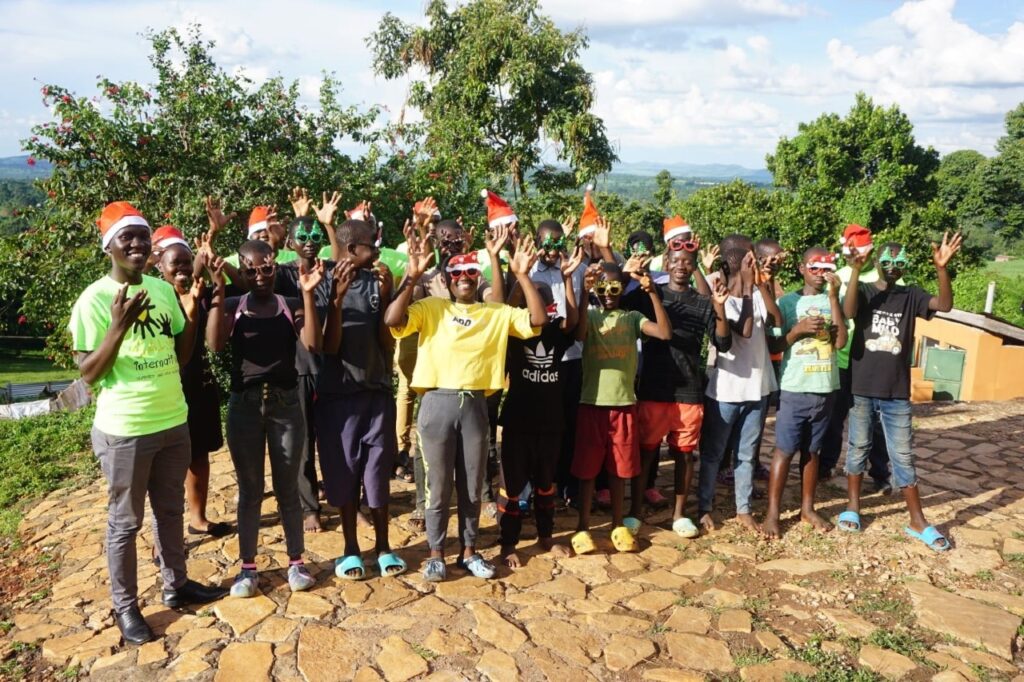 a large group of children and SALVE staff members smiling, wearing Christmas hats and glasses and waving their hands in the air