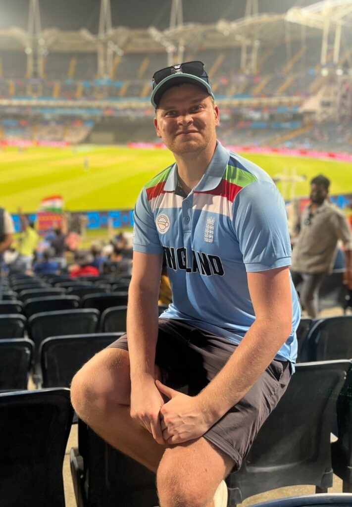 Lucas Mee, SALVE's CEO, is smiling at the camera and sitting casually at a cricket game.