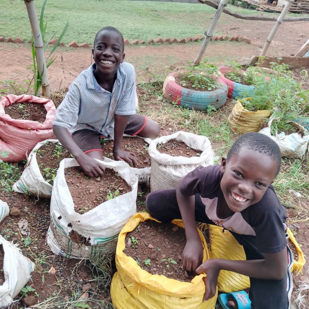 two boys smiling and looking at the camera while sack gardening
