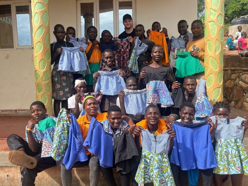 a group of young people from the SALVE tailoring programme holding up their garments