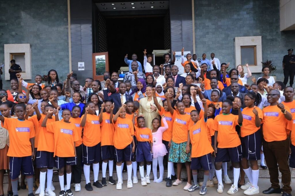 A large group of people smiling for the camera and cheering outside inside the Ugandan Parliament.