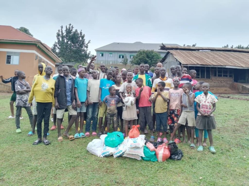 A large group of children are standing behind some donated items.