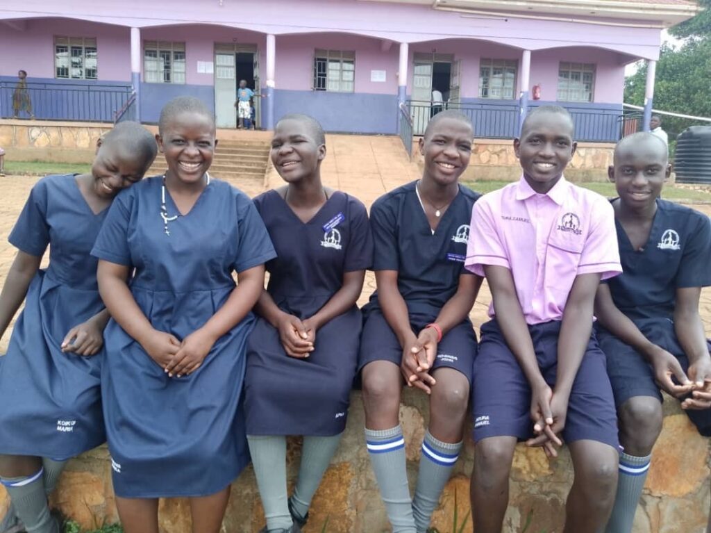 A group of young people are wearing school uniforms, sitting on a wall and smiling for the camera. They look happy.