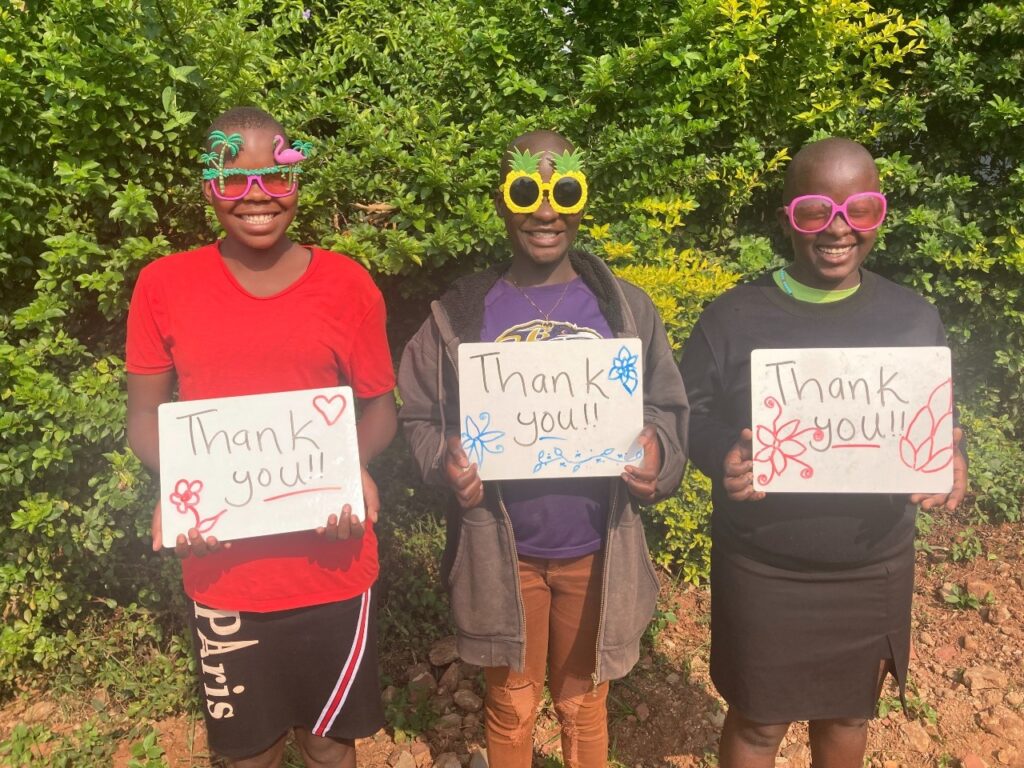 Three children holding signs saying thank you. The children are wearing brightly coloured sunglasses.