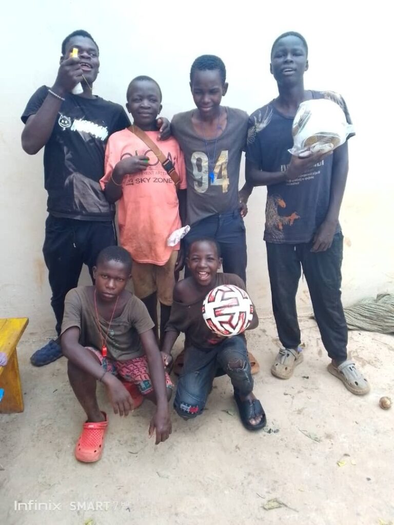 Six boys are posing for the camera. Two are holding footballs.