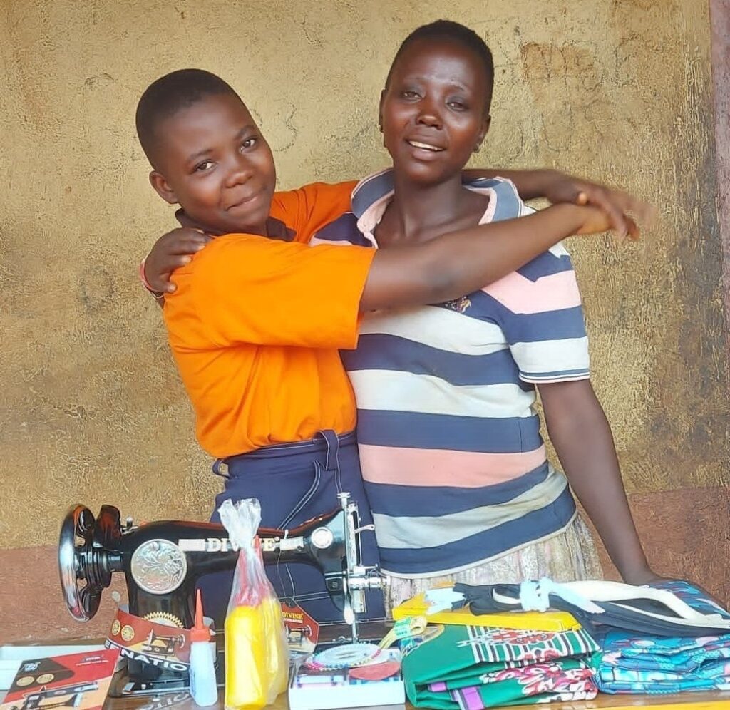 A daughter has her arms around her mum, standing in front of a table with sewing paraphernalia on